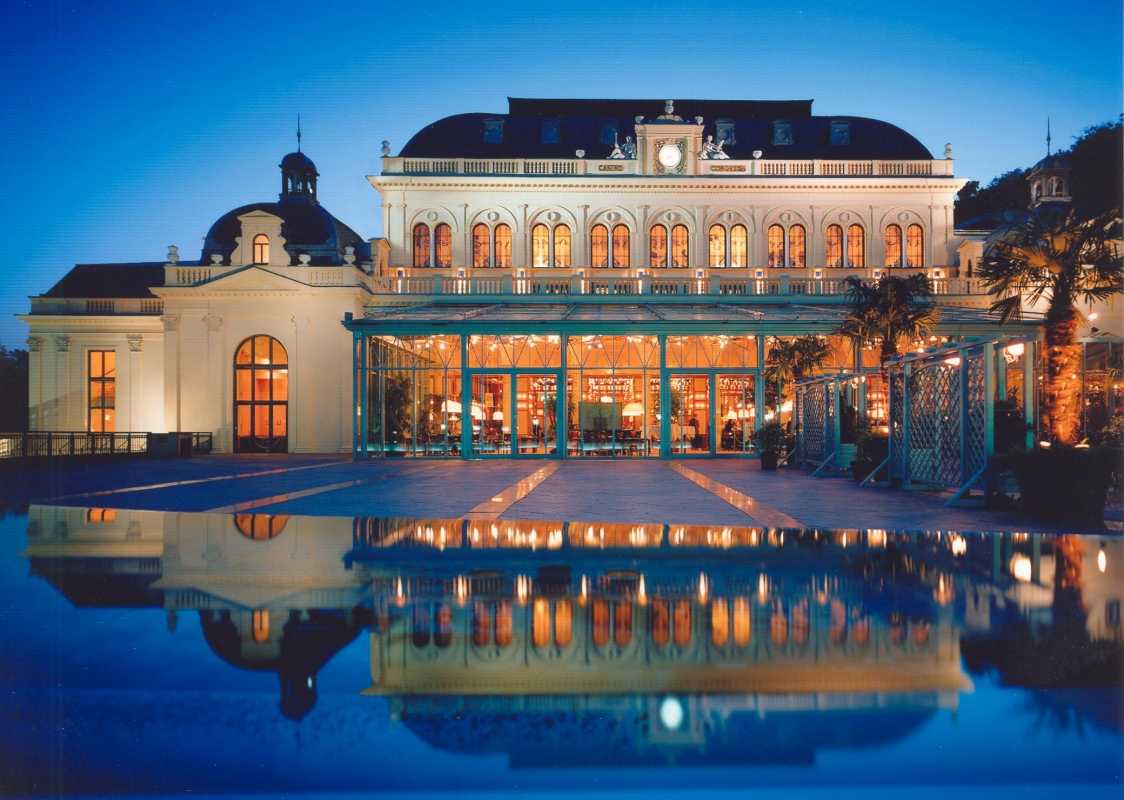 Beleuchtete Fassade des Kurhauses Baden-Baden bei Nacht mit Spiegelung im Wasser.