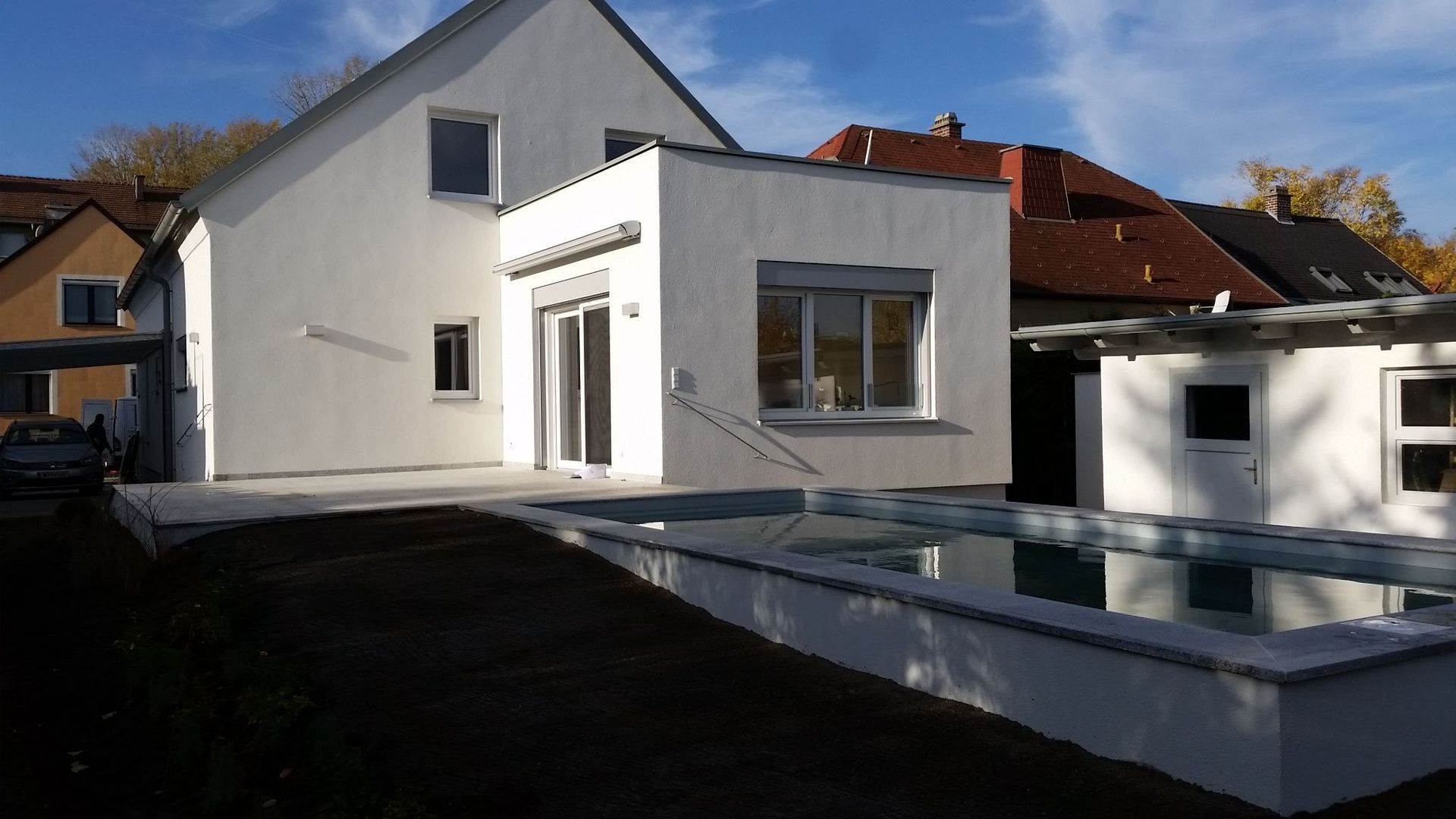 Moderner weißer Hausanbau mit Flachdach und vorgelagertem, gemauerten Swimmingpool im Garten.