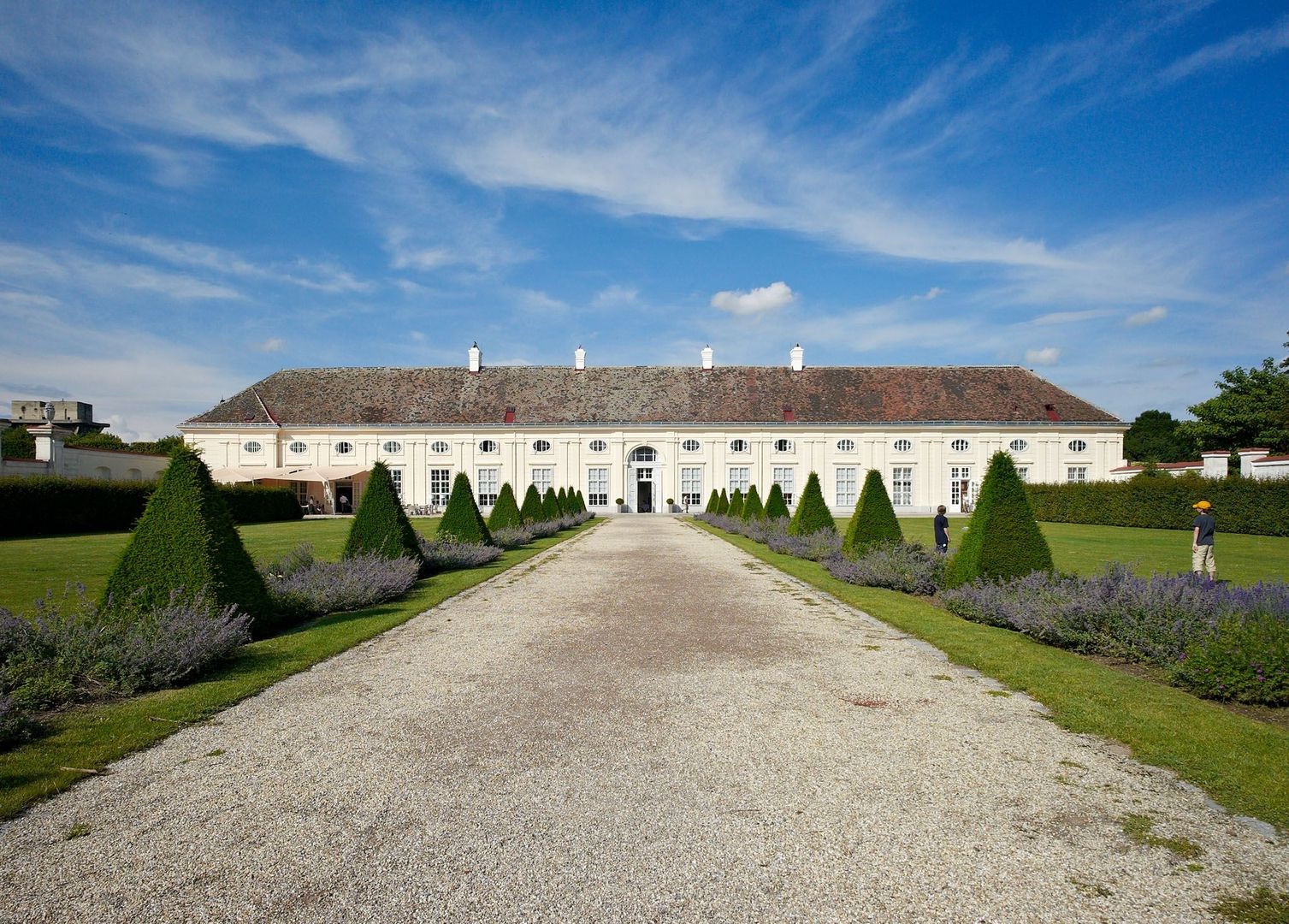 Barocker Schlossbau der Porzellanmanufaktur Augarten mit symmetrischer Gartenanlage und kegelförmig zugeschnittenen Hecken.