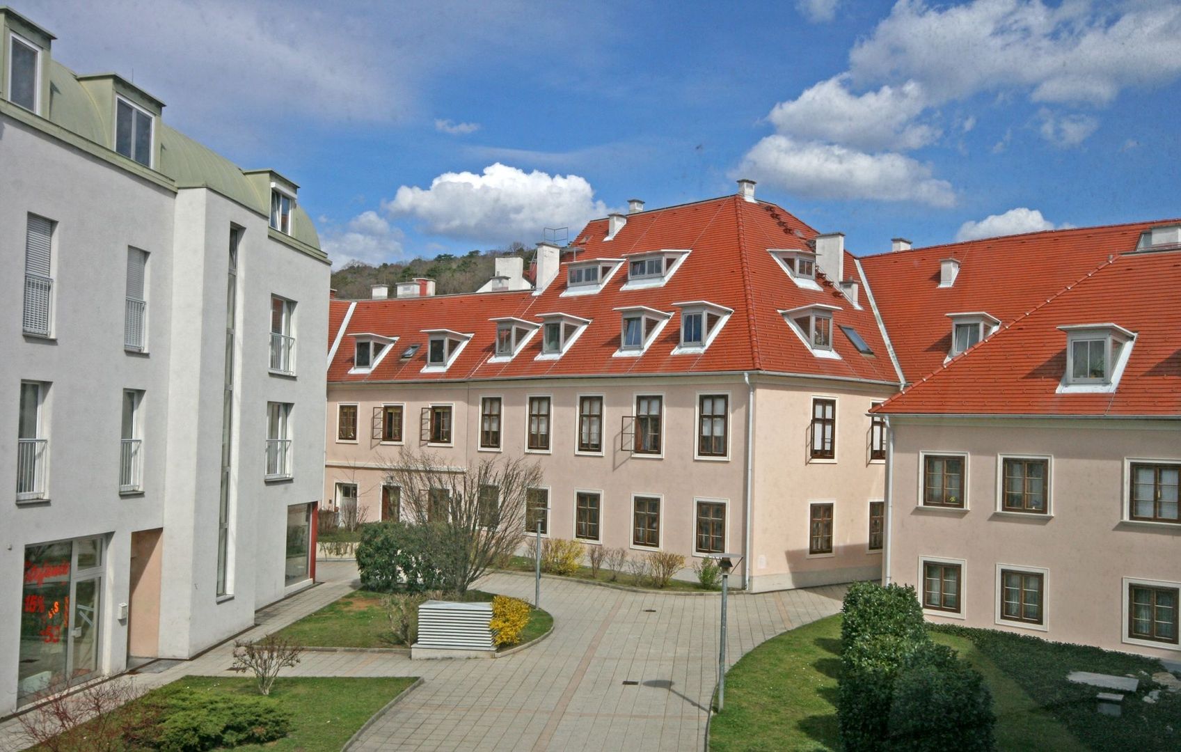 Foto eines Innenhofs einer modernen Wohnanlage mit gepflasterten Wegen, Grünflächen und Gebäuden mit markanten roten Ziegeldächern und Dachgauben.