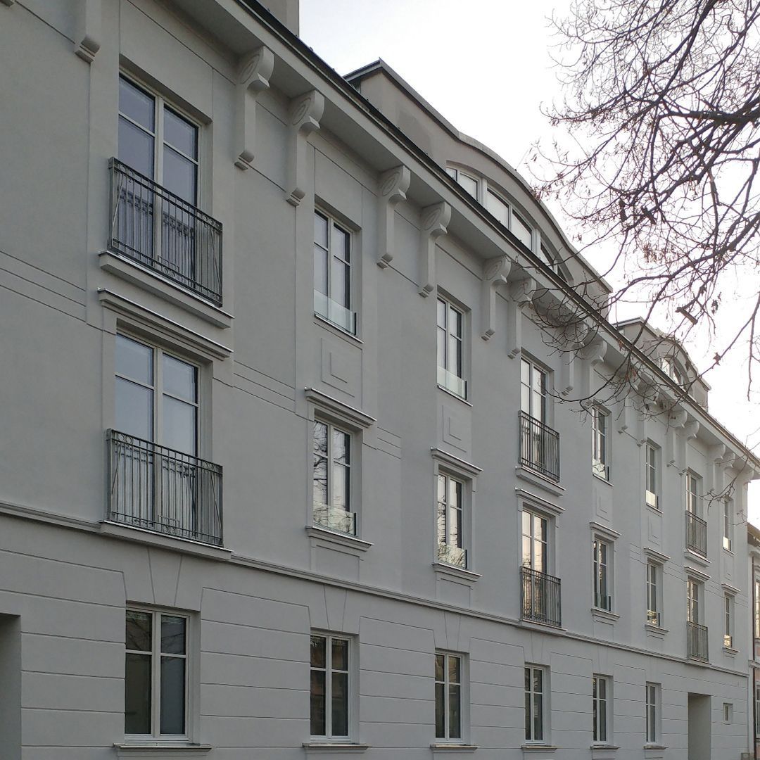 Foto einer sanierten Altbaufassade mit hellgrauem Putz, französischen Balkonen mit schwarzen Metallgittern und dekorativen Gesimsen unter der Dachkante.