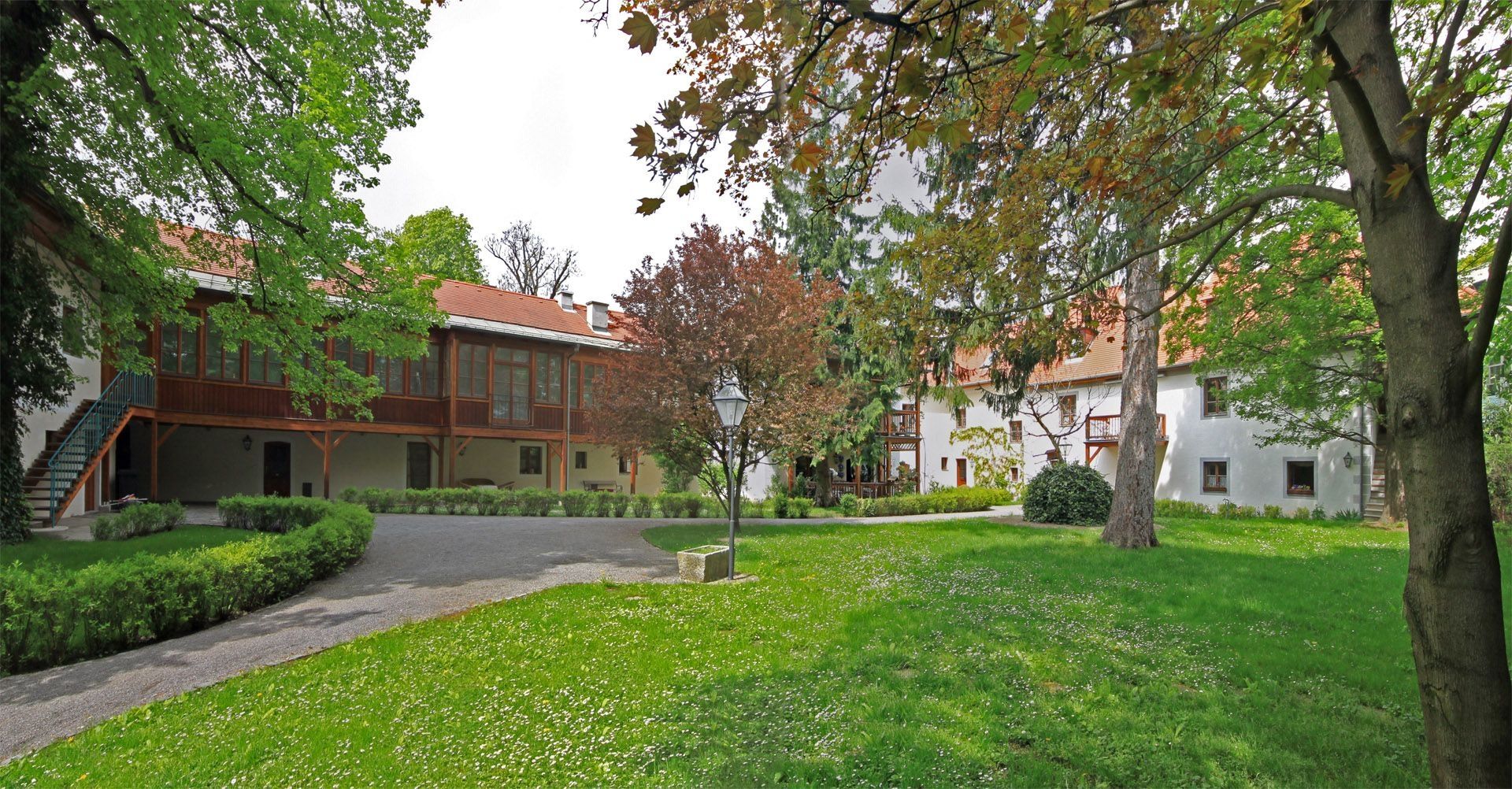 Foto eines begrünten Innenhofs mit Rasenflächen und altem Baumbestand, umgeben von revitalisierten historischen Gebäuden mit Holzelementen und Laubengängen.